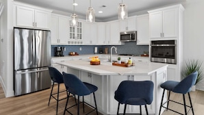 A modern kitchen with white cabinets, stainless steel appliances, and a central island with bar stools. - Arbor-Lyn * 4BR Luxury House, Sleeps 10 (Rehoboth Beach)
