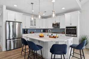 A modern kitchen with white cabinets, stainless steel appliances, and a central island with bar stools.