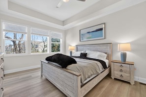 A bedroom with a bed, bedside tables, a window with blinds, a ceiling fan, and a painting on the wall.