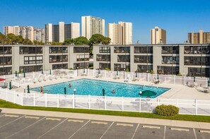 Ein modernes Hotel mit einem zentral gelegenen Schwimmbad, umgeben von weißen Zäunen und Balkonen.