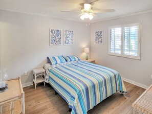 Quarto com cama, mesa de cabeceira, luminária, cadeira e janela com persianas.