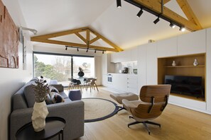 Een moderne woonkamer met een grijze bank, een houten stoel, een salontafel en een tv op een houten plank.