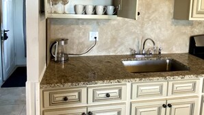 A kitchen with white cabinets, a granite countertop, a sink, and a coffee maker. - Open concept, 2-level apartment with scenic view (Gloucester)