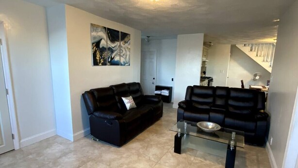 A spacious living room with two black sofas, a glass coffee table, and a large abstract painting on the wall. - Open concept, 2-level apartment with scenic view (Gloucester)