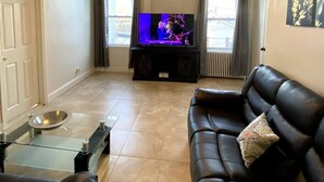 A living room with a black leather sofa, a glass coffee table, a TV on a stand, and a painting on the wall. - Open concept, 2-level apartment with scenic view (Gloucester)