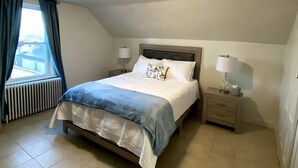 A bedroom with a bed, bedside tables, a radiator, and a window with curtains. - Open concept, 2-level apartment with scenic view (Gloucester)