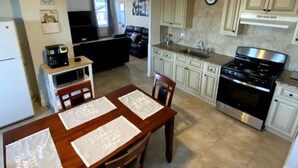 A compact kitchen with white cabinets, a stove, and a dining area with a table set for four. - Open concept, 2-level apartment with scenic view (Gloucester)