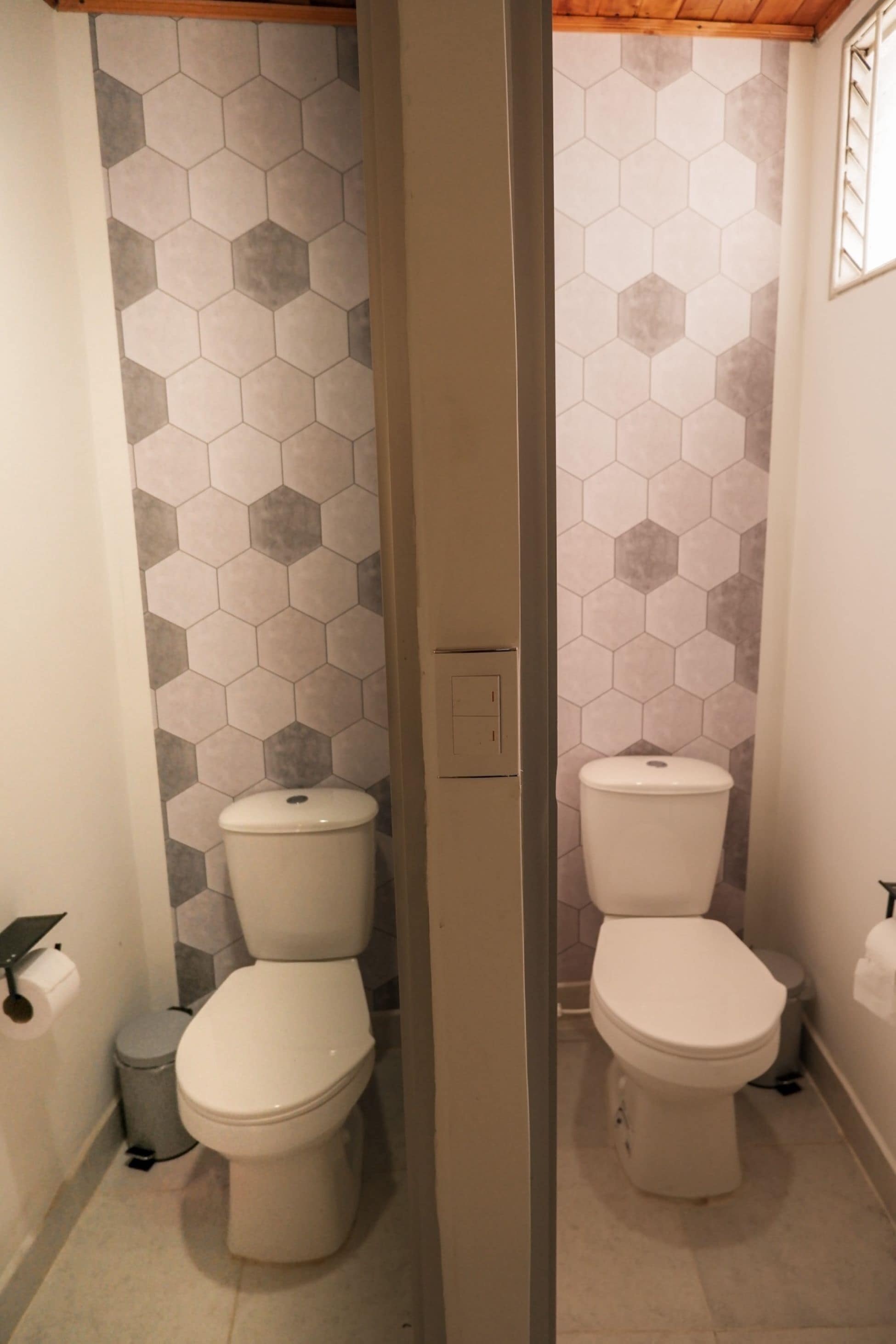 A bathroom with two toilets, a toilet paper holder, and a trash can.