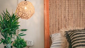 A bedroom with a bed, a bedside table with two potted plants, a hanging light fixture, and a textured wall panel. - De Requka (Pereira)