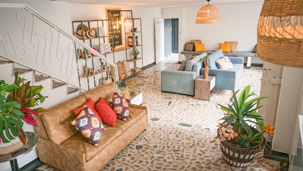 A spacious living area with a staircase, a sofa with patterned cushions, and a dining area with a blue sofa and orange cushions. - De Requka (Pereira)