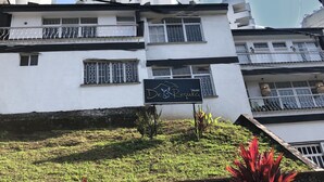 A hostel sign with a mountain and bird logo, surrounded by greenery and a white building with balconies.