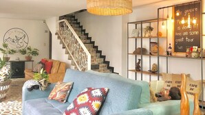 A cozy living room with a blue sofa, a woven pendant light, a staircase, and a wall with a chalkboard sign. - De Requka (Pereira)