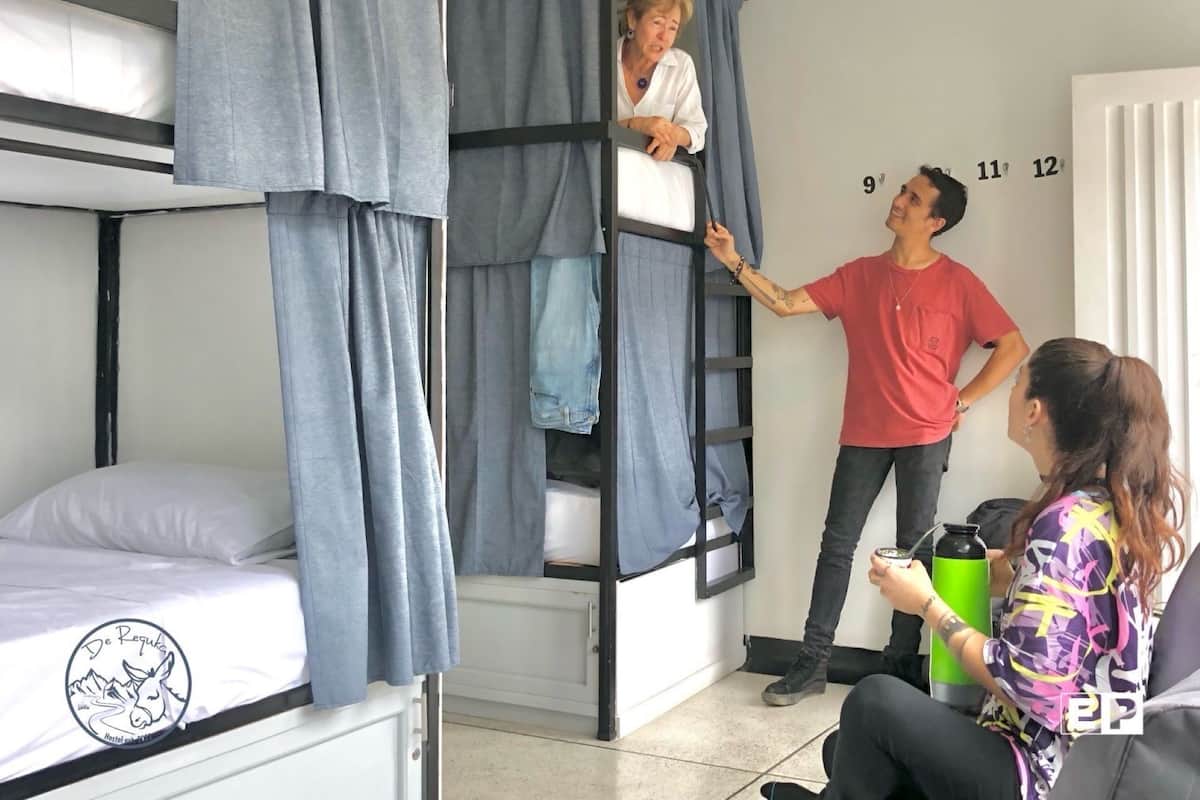 A dormitory room with bunk beds, a ladder, and a person climbing the ladder.
