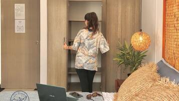 Una habitación con una cama, una computadora portátil, una planta y una lámpara de pared.
