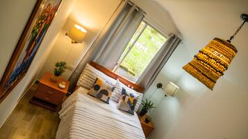 Un dormitorio con cama, mesitas de noche, una ventana con cortinas, una lámpara colgante y un cuadro en la pared.
