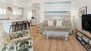 A modern living room with a large painting of the ocean, a gray sofa, and a stone bench. - Always Channel-On Muskegon Channel, walk to lighthouse, beach, the DECK & swim.  (Muskegon)