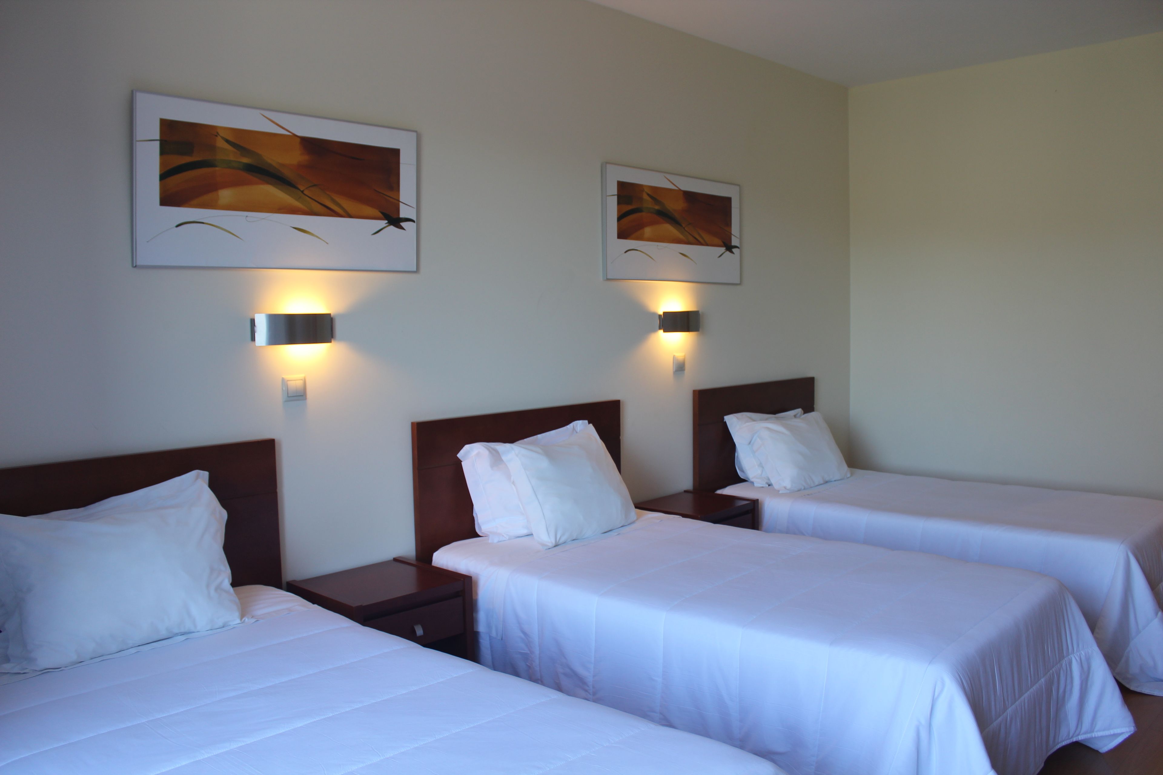 A hotel room with two single beds, each with a wooden headboard and white bedding. There are two wall-mounted light fixtures above the beds.
