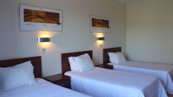 A hotel room with two single beds, each with a wooden headboard and white bedding. There are two wall-mounted light fixtures above the beds.