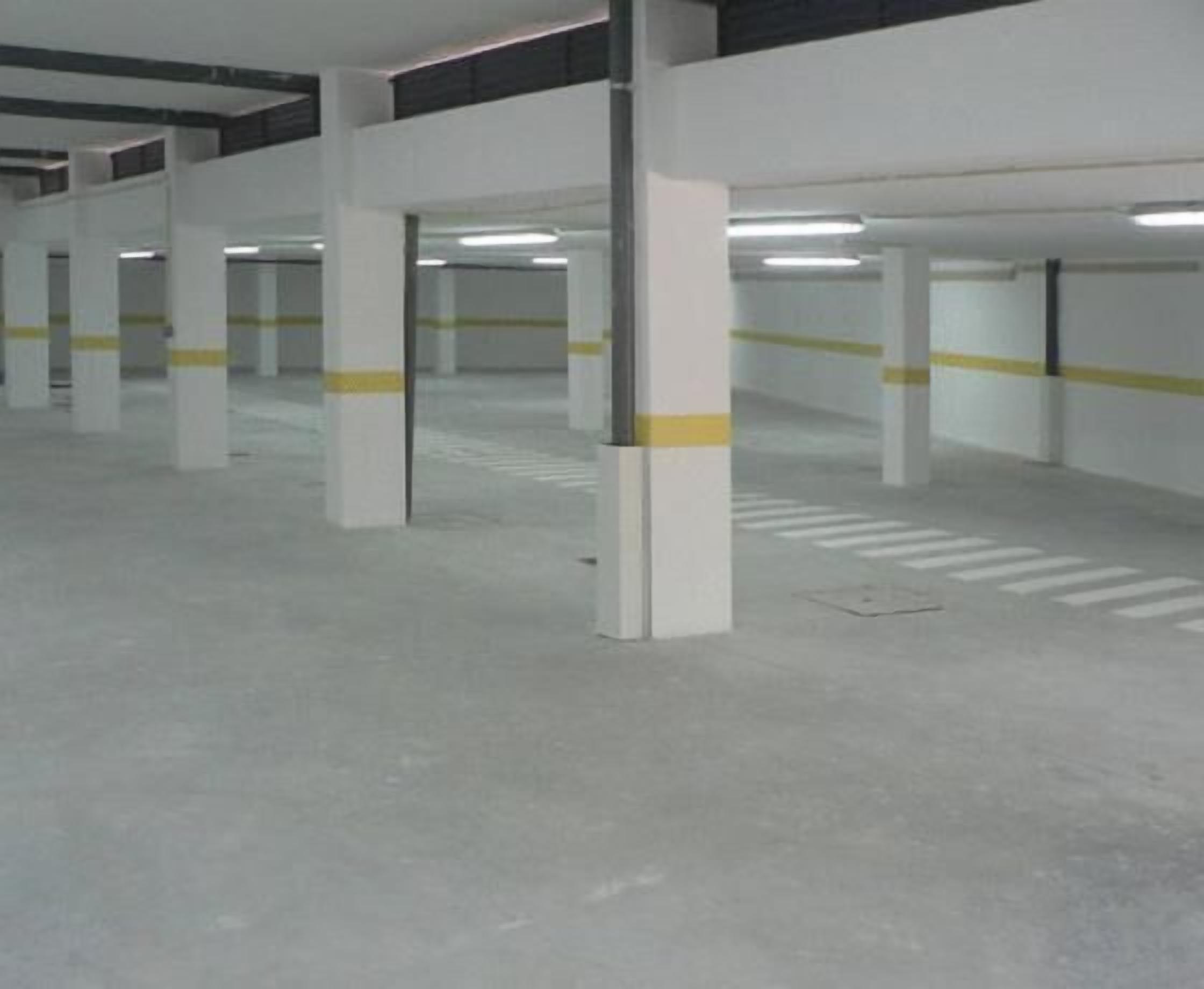An indoor parking garage with white pillars and yellow lines marking parking spaces.