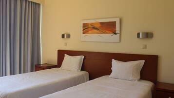 A hotel room with two beds, a painting on the wall, and a window with curtains.
