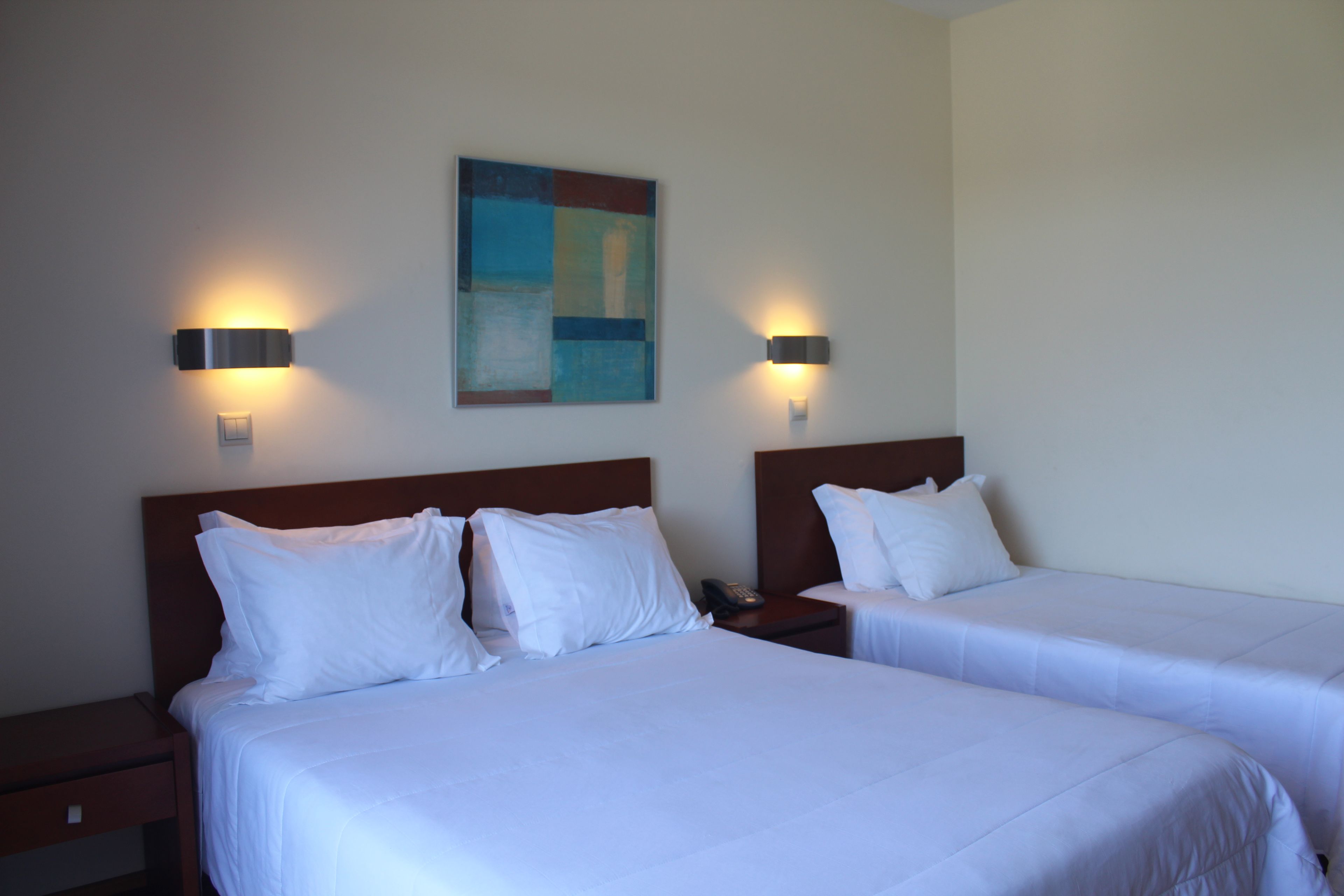 Ein Hotelzimmer mit zwei Betten, jeweils mit weißer Bettwäsche und Kopfteilen, sowie zwei wandmontierten Leuchten.