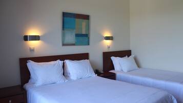 Habitación de hotel con dos camas, cada una con ropa blanca y cabeceros, y dos lámparas fijadas a la pared.