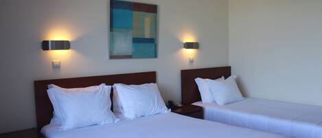 Ein Hotelzimmer mit zwei Betten, jeweils mit weißer Bettwäsche und Kopfteilen, sowie zwei wandmontierten Leuchten.