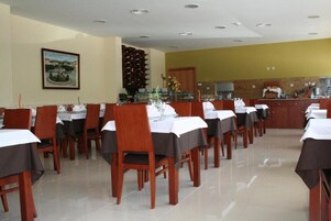Un restaurante con varias mesas y sillas, una zona de cocina y un cuadro en la pared.