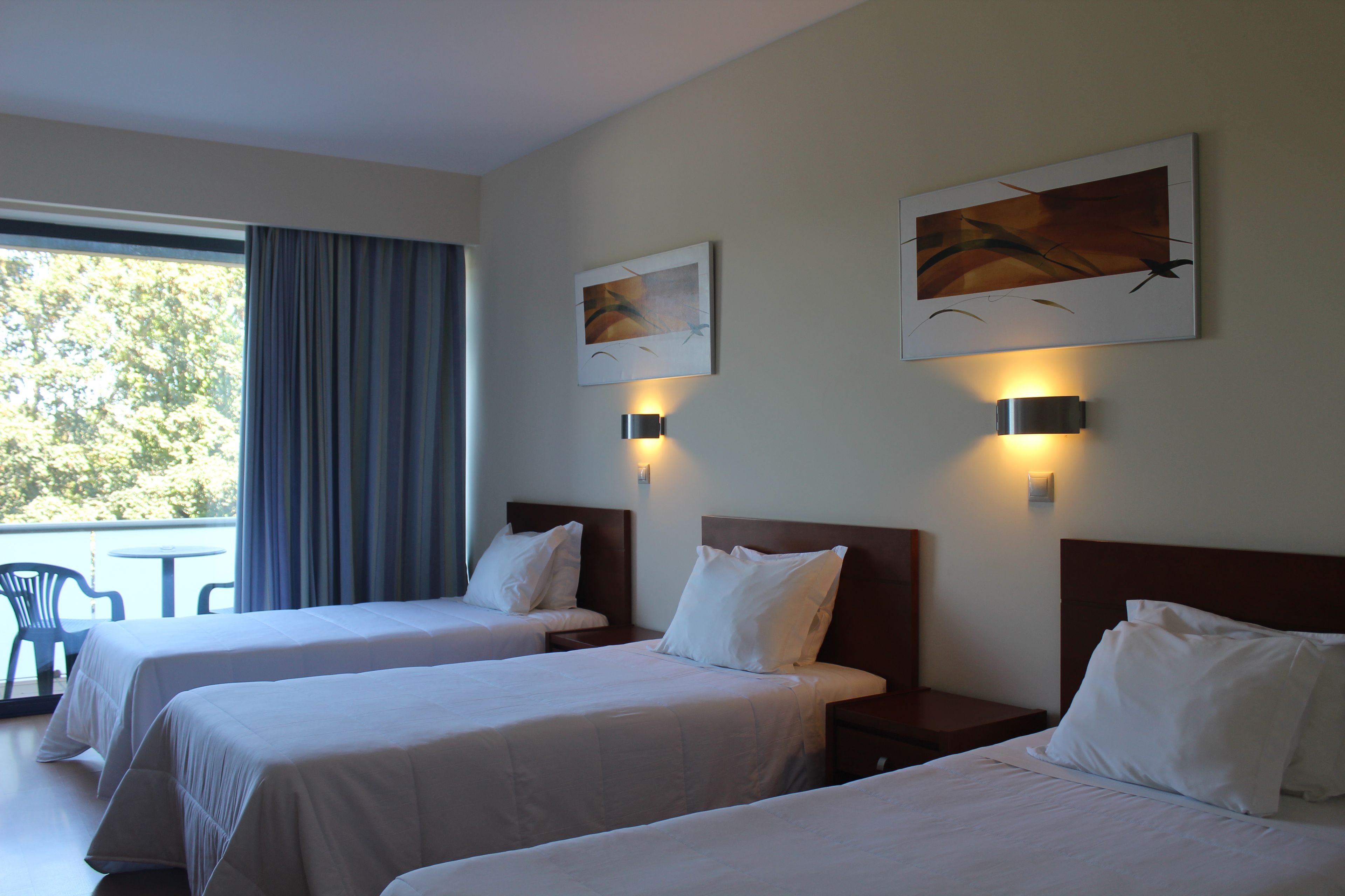 Una habitación de hotel con dos camas, un ventanal con cortinas y dos lámparas fijadas a la pared.