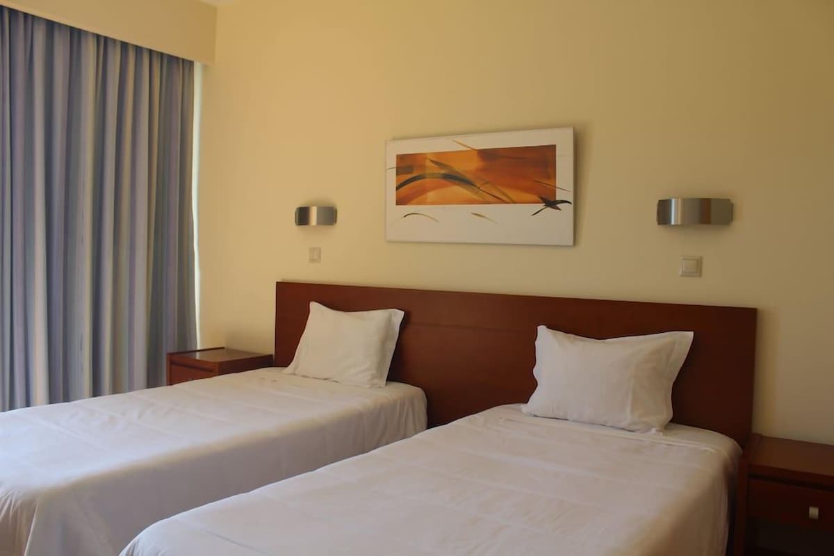 Une chambre d’hôtel avec deux lits, un tableau au mur et une fenêtre avec des rideaux.