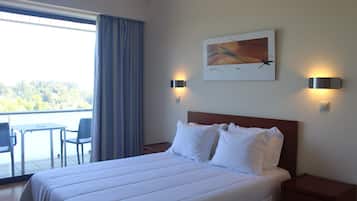 Une chambre d’hôtel avec un lit, deux lampes de chevet, un tableau au mur, une fenêtre avec des rideaux et une vue sur l’extérieur.