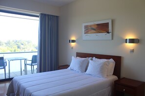 A hotel room with a bed, two bedside lamps, a painting on the wall, a window with curtains, and a view of the outdoors. - Hotel Dom Afonso (Monção)