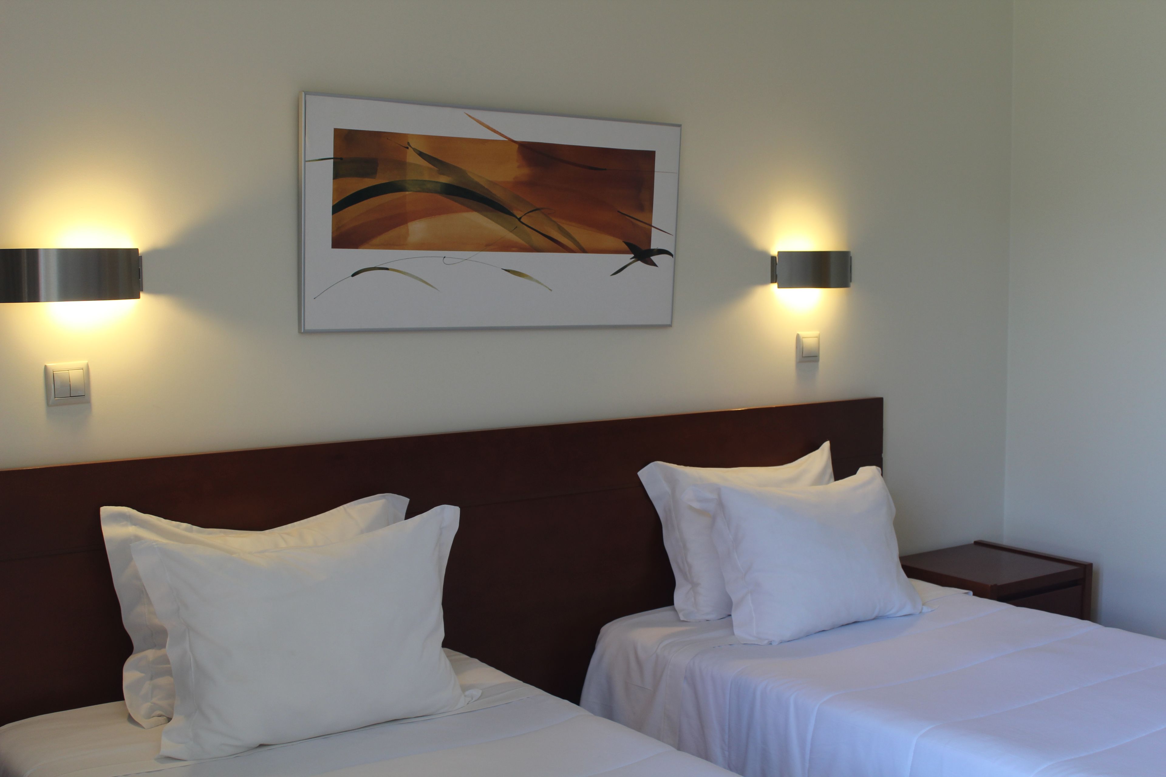 Una habitación de hotel con dos camas, cabecero y un cuadro colgado en la pared.
