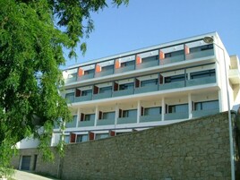 Un hotel de varios pisos con balcones, una pared de piedra en primer plano y un cielo azul despejado.