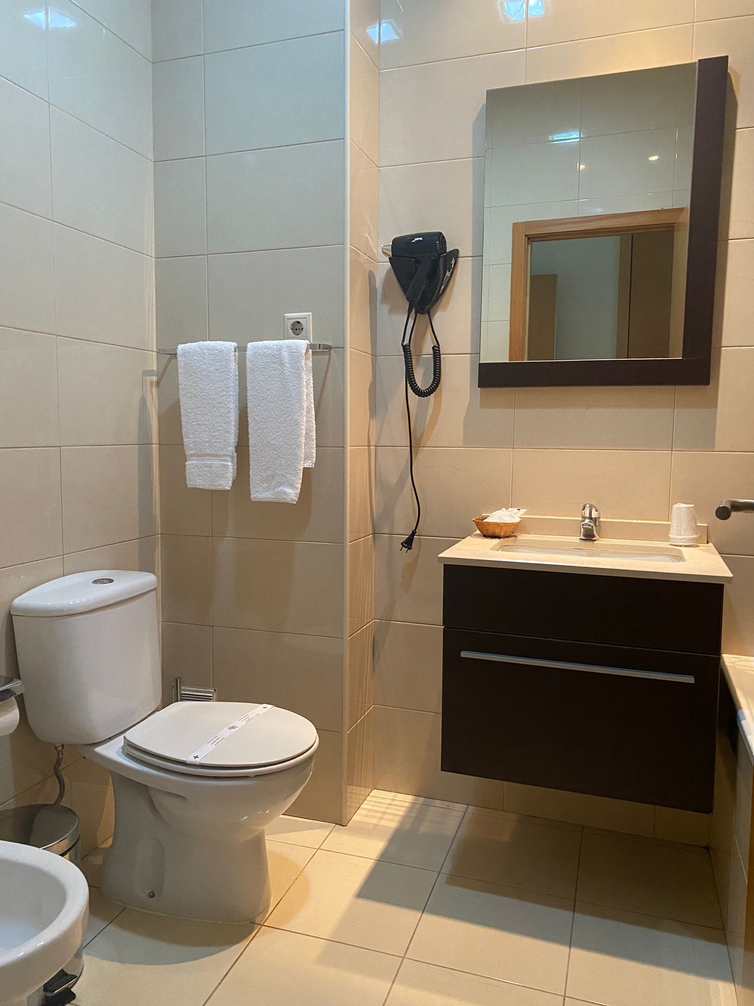 A bathroom with a toilet, bidet, sink, and a hairdryer mounted on the wall.