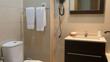 Un baño con inodoro, bidé, lavabo y un secador de pelo montado en la pared.