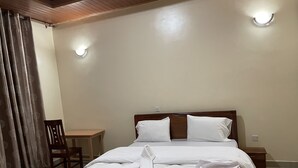 A neatly made bed with white linens and towels, a wooden headboard, a small wooden table, and a chair. - M Safari Club (Kigali)