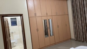 A room with a large wardrobe, a bathroom with a toilet and sink, and a bed with white linens. - M Safari Club (Kigali)