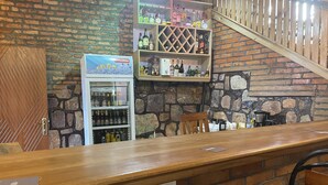 A bar area with a wooden counter, shelves with bottles, a refrigerator, and a stone wall backdrop. - M Safari Club (Kigali)