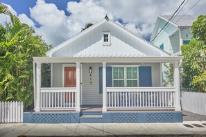 A small, single-story house with a porch, white siding, and a blue door.