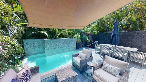 A pool area with a hot tub, lounge chairs, and a table.