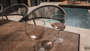 Un coin de paradis au bord de la piscine, avec deux fauteuils en osier et une table, un verre de vin et la piscine elle-même.