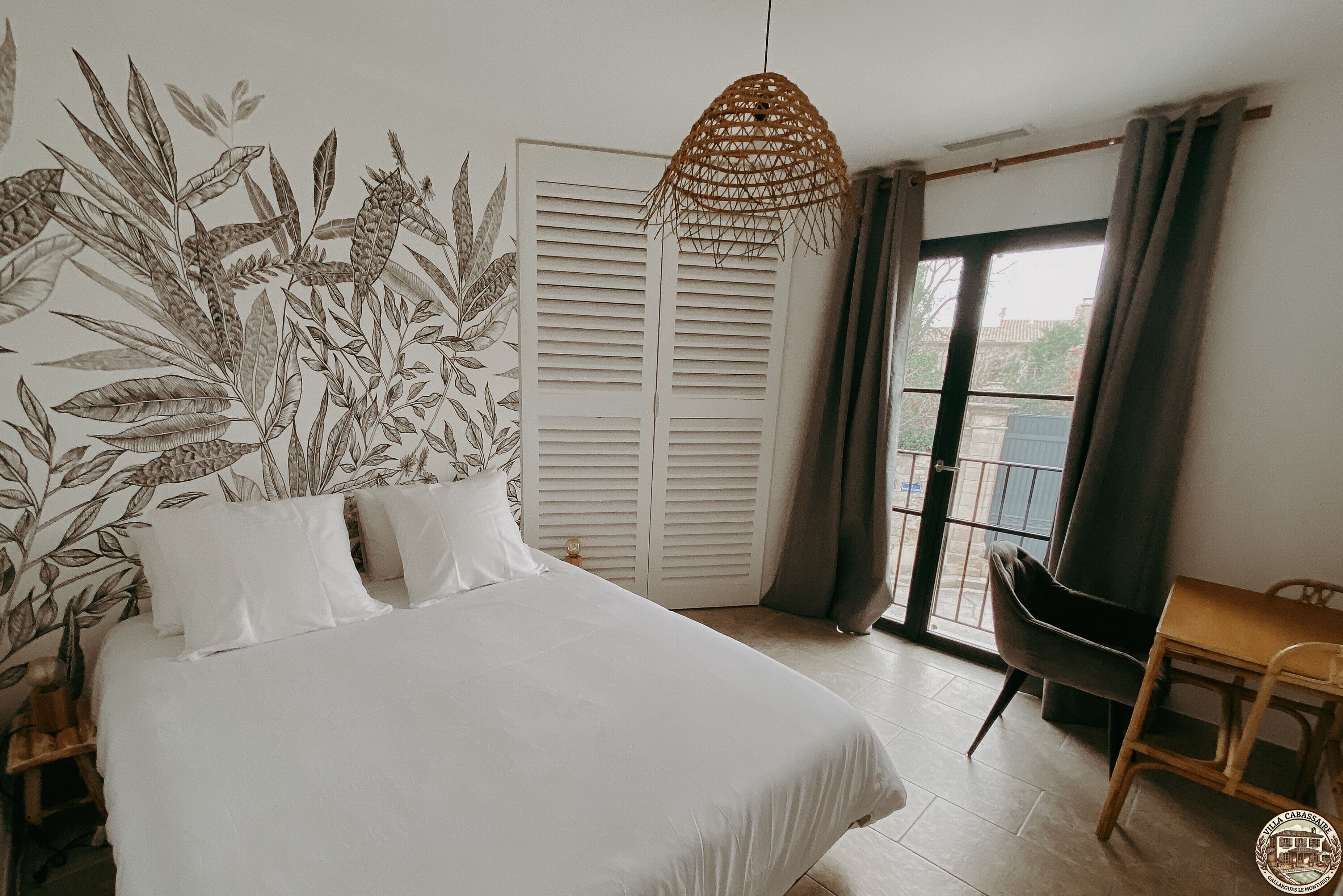 Un dormitorio con cama, lámpara colgante, armario, silla y vista por la ventana.