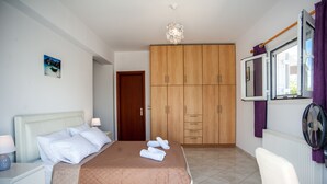 Un llit ben fet amb llençols marrons, un armari de fusta, una cadira blanca i una taula de nit amb una làmpada.