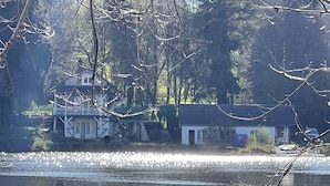 En fastighet vid en sjö med ett hus som har en balkong och ett litet förråd.