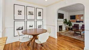 A dining area with a round wooden table and white chairs, framed black-and-white photographs on the wall, and a wooden floor. - Vulcan View Cottage (Birmingham)