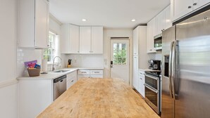 A modern kitchen with white cabinets, a wooden countertop, stainless steel appliances, and a window providing natural light. - Vulcan View Cottage (Birmingham)