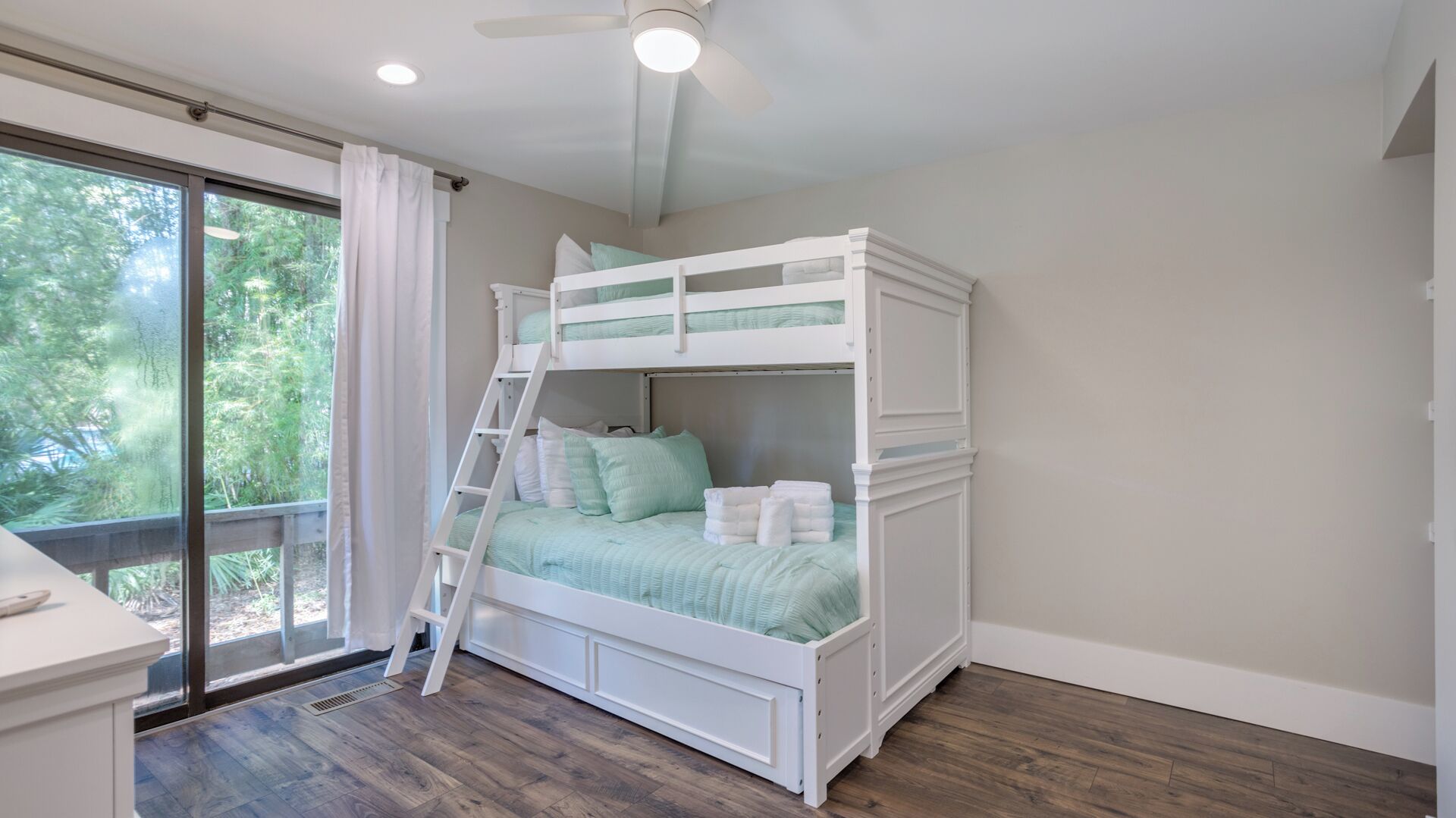 A bunk bed room with a ladder, a window with curtains, and a ceiling fan.