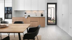 A modern kitchen with white cabinets, a wooden countertop, and a black chair. There is a dining table with a bowl of fruit and a potted plant. - Villa Sealine in Vinkuran (Vinkuran)