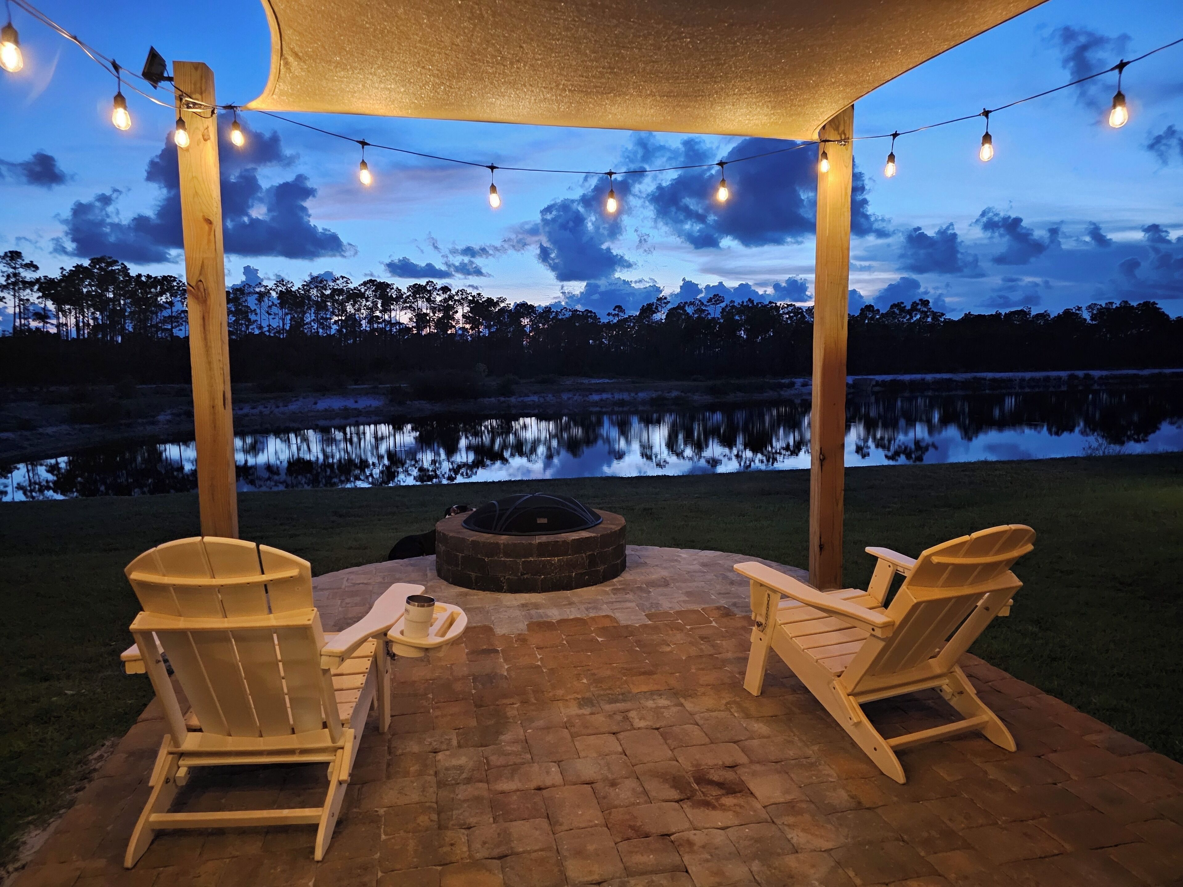 An outdoor patio with two Adirondack chairs, a fire pit, and string lights.